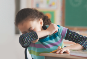 A Kleenex box, a tablet, a stack of books, and a backpack full of school supplies sit on a table.