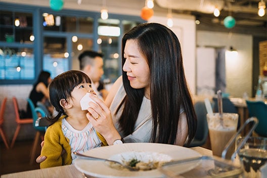 Woman helping child using Kleenex® Trusted Care® Tissue to clean up mess from a sneeze